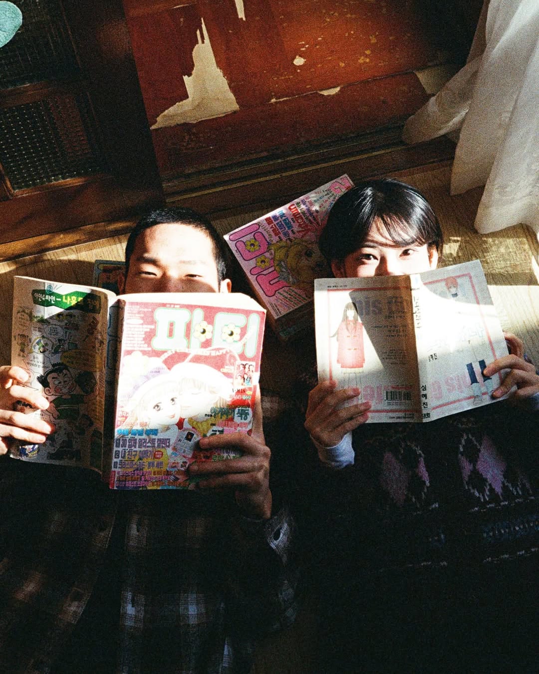 펜탁스17 PENTAX17로 촬영한 커플 스냅. 커플이 만화책으로 입을 가리며 카메라를 응시하고 있다.